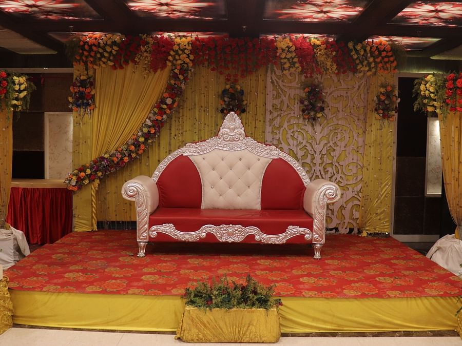 A stage with a cushioned sofa, a well-decorated dais, and an elegantly designed background at Hotel Uday Palace.