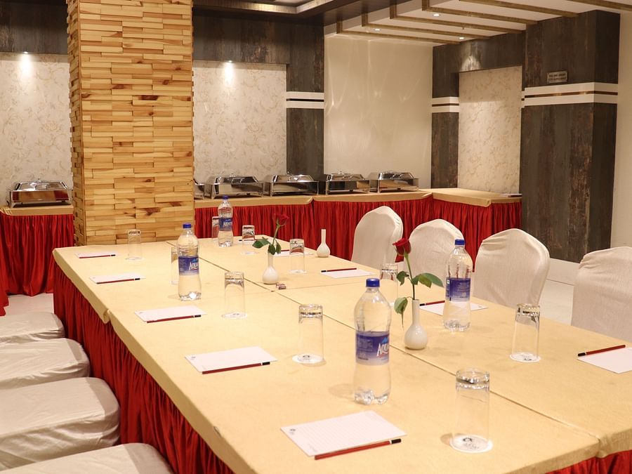 A close-up view of a large table with chairs on both sides, set with stationery and water bottles at Hotel Uday Palace.
