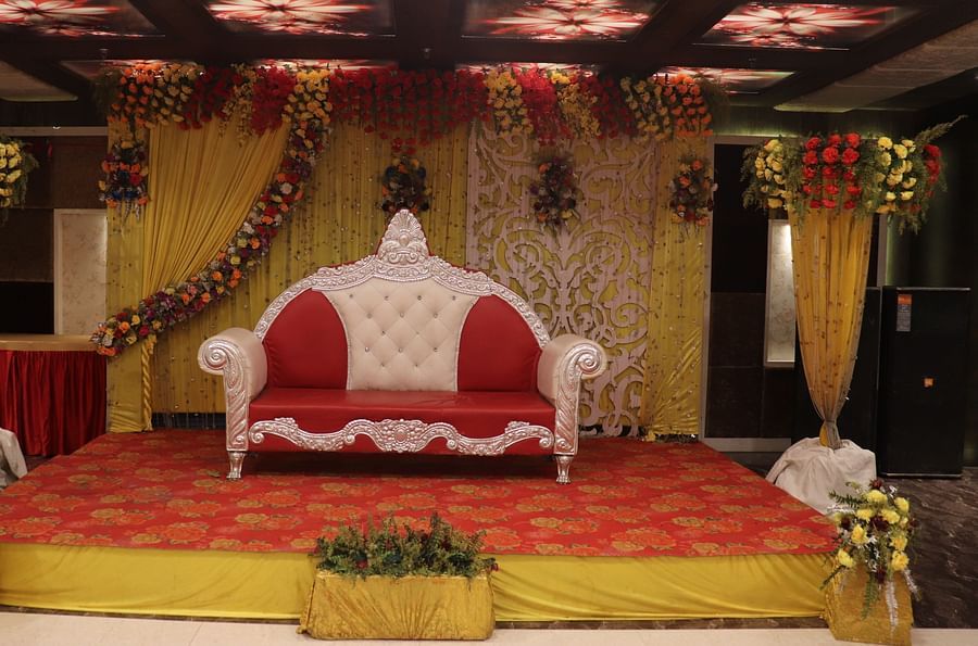 A stage with a cushioned sofa, a well-decorated dais, and an elegantly designed background at Hotel Uday Palace.