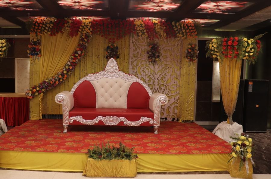 An ornate wedding stage setup with golden decor and red seating for 2 people, at one of the finest banquet halls in Varanasi - Hotel Uday Palace.