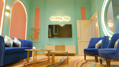 A modernly furnished waiting area or lounge at The Gaurs Sarovar Premiere, with blue armchairs and a coffee table on a patterned rug.