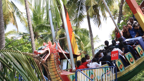 A vibrant dragon-themed roller coaster filled with excited riders, weaving through palm trees and towering structures - The Black Thunder