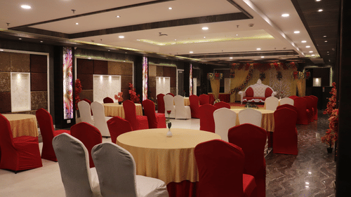 A banquet hall view from the end, featuring elegantly arranged tables and chairs facing the stage.