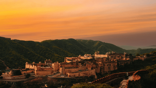 An image of Amber Fort featuring large architectural building surrounded by lush green hills 