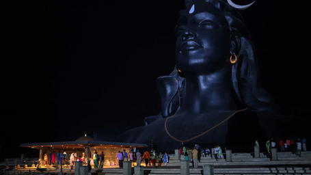 A humongous black shiva statue packed with tourists with a night sky background.