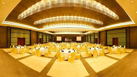 Spacious banquet hall with round tables, elegant decor, and warm lighting at GRT Hotels