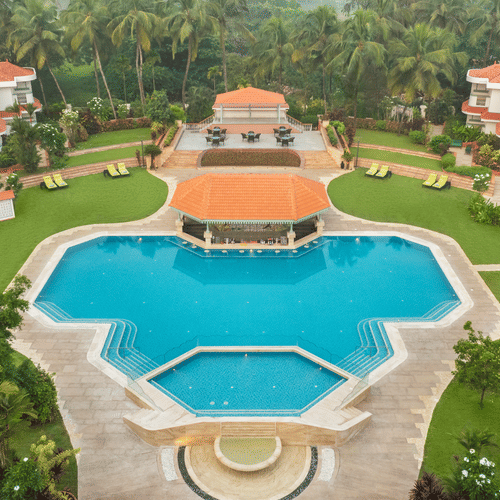 Aerial view of a large resort with a central swimming pool and landscaped gardens at Heritage Village Resorts & Spa | South Goa Hotel near Beach