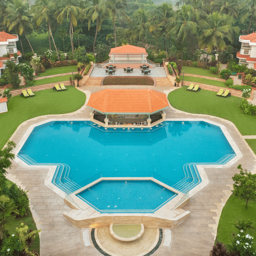 Aerial view of a large resort with a central swimming pool and landscaped gardens at Heritage Village Resorts & Spa | South Goa Hotel near Beach