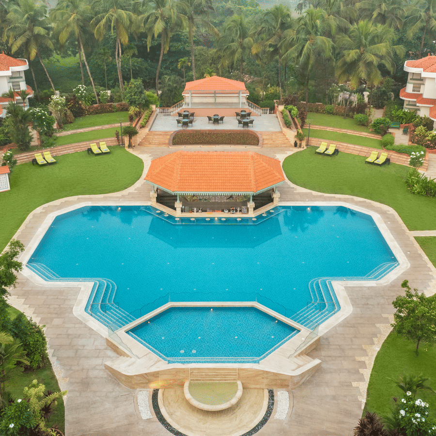 Aerial view of a large resort with a central swimming pool and landscaped gardens | South Goa Hotel near Beach
