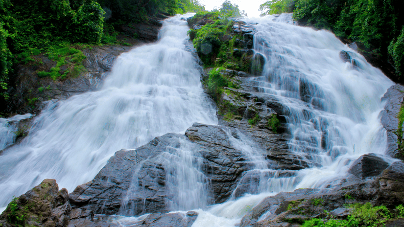 A waterfall cascading down a steep, rocky incline covered with dense green foliage on both sides.