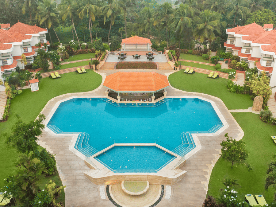 Aerial view of a large resort with a central swimming pool and landscaped gardens at Heritage Village Resorts & Spa | South Goa Hotel near Beach