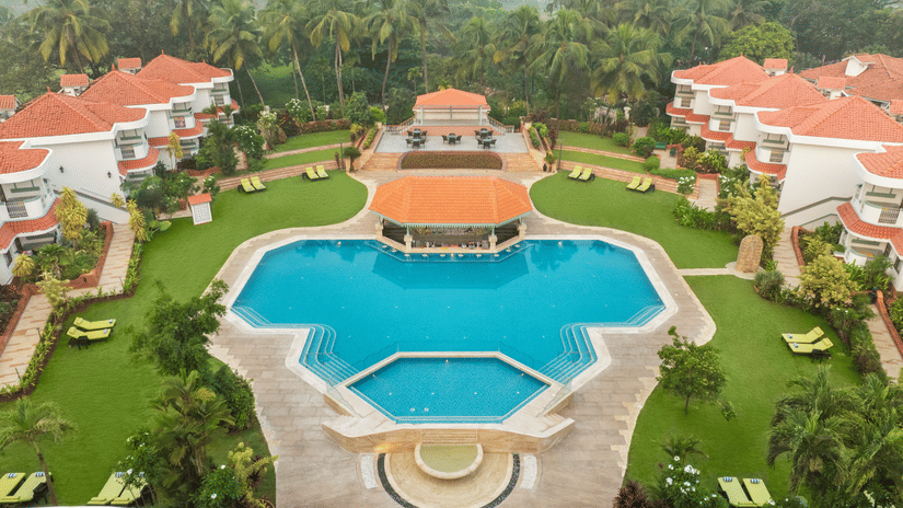 Aerial view of a large resort with a central swimming pool and landscaped gardens | South Goa Hotel near Beach