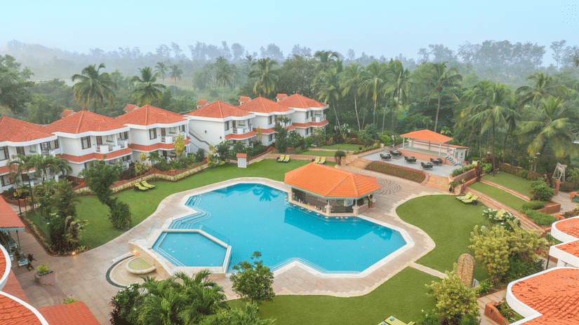 Aerial view of Heritage Village Resorts & Spa, Goa, with the swimming pool in view and lush greenery surrounding the buildings.