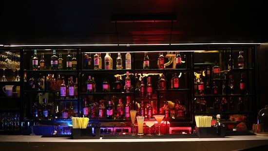 A vibrant and well-stocked bar shelf with illuminated liquor bottles and signature cocktails on the counter at Sarovar Portico, Sonipat. 