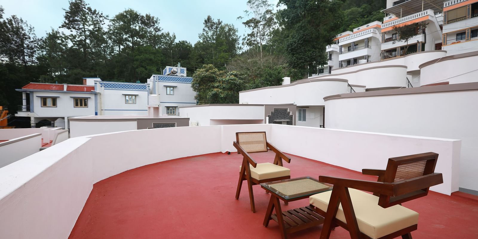 The terrace area at the Terrace Cottage with an outdoor seating area with a backdrop of lush green trees and a serene blue sky in the background at WOW Naturefull Resorts, Yercaud.