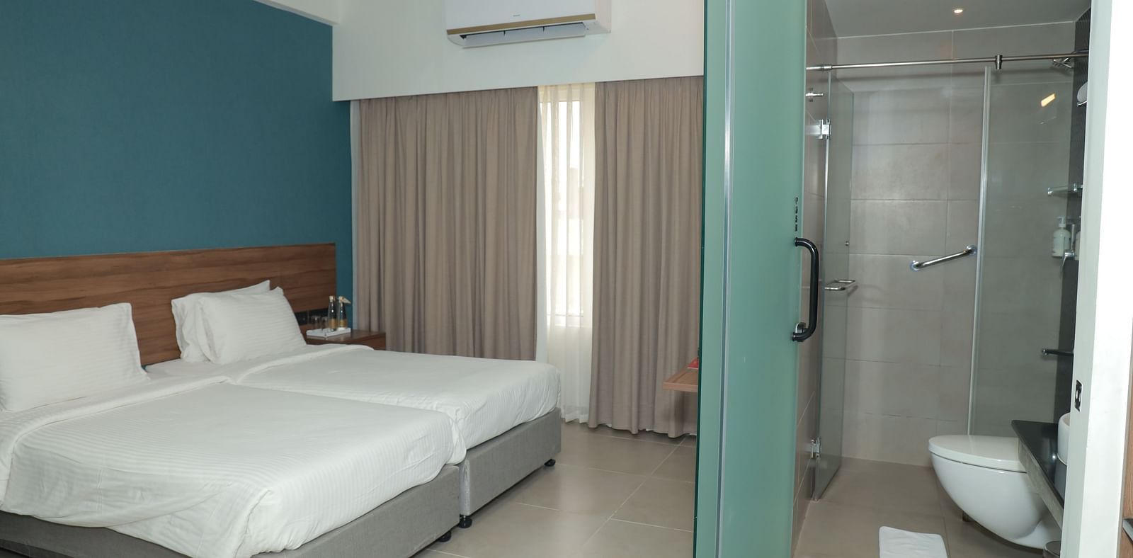 A view of twin beds arranged in our Deluxe Room, with a contemporary shower area in front, showcasing modern amenities - Regency Tuticorin by GRT Hotels