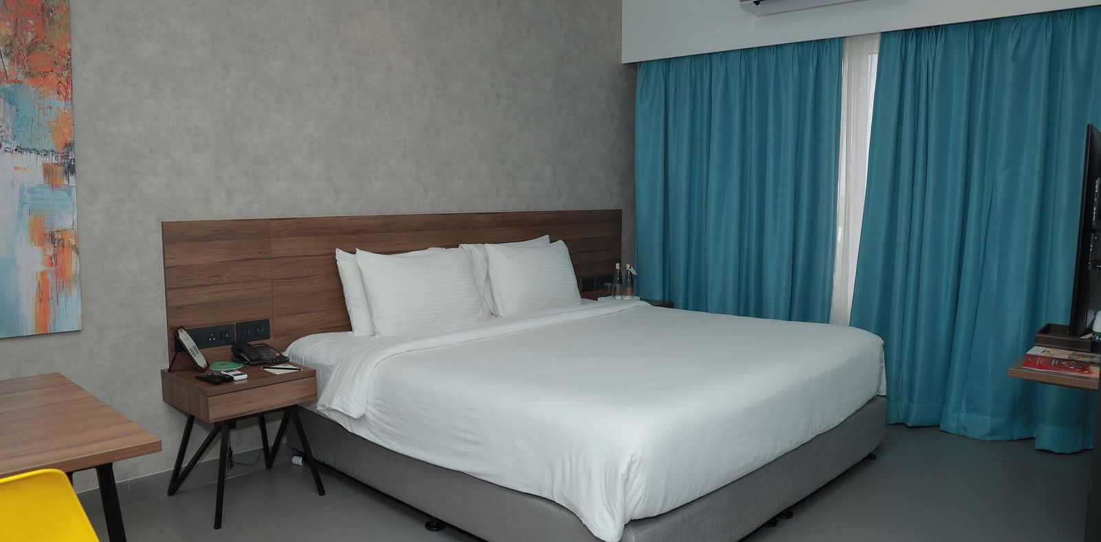 An image of a king size bed in our Deluxe Room with a wooden chair placed beside it - Regency Tuticorin by GRT Hotels
