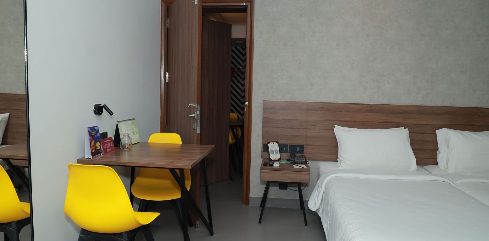 An image of twin beds placed beside a table with two yellow chairs in our Deluxe Rooms in Tuticorin - Regency Tuticorin by GRT Hotels