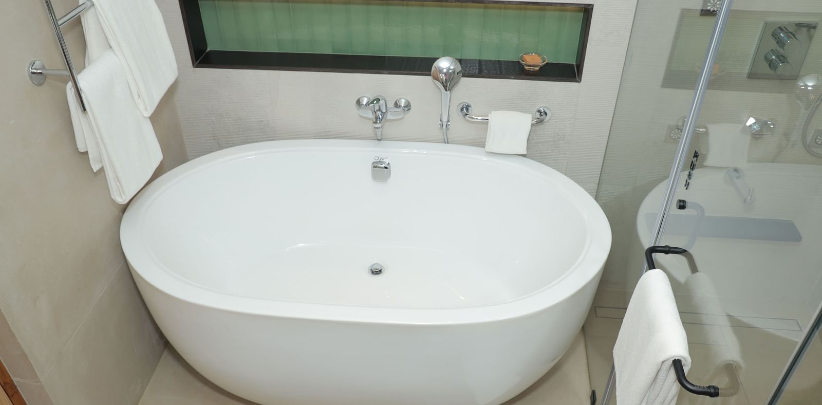 A clean bathroom with a bathtub and towels hanging on a rack attached to the shower cubicle door - Regency Tuticorin by GRT Hotels