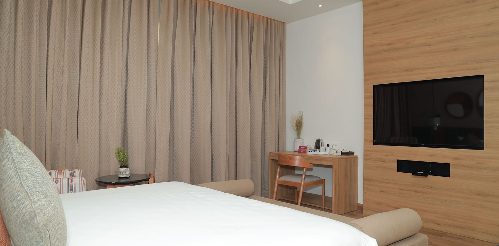 An image of a bed with a pillow placed in front of a wall-mounted television, and a work desk nearby - Regency Tuticorin by GRT Hotels