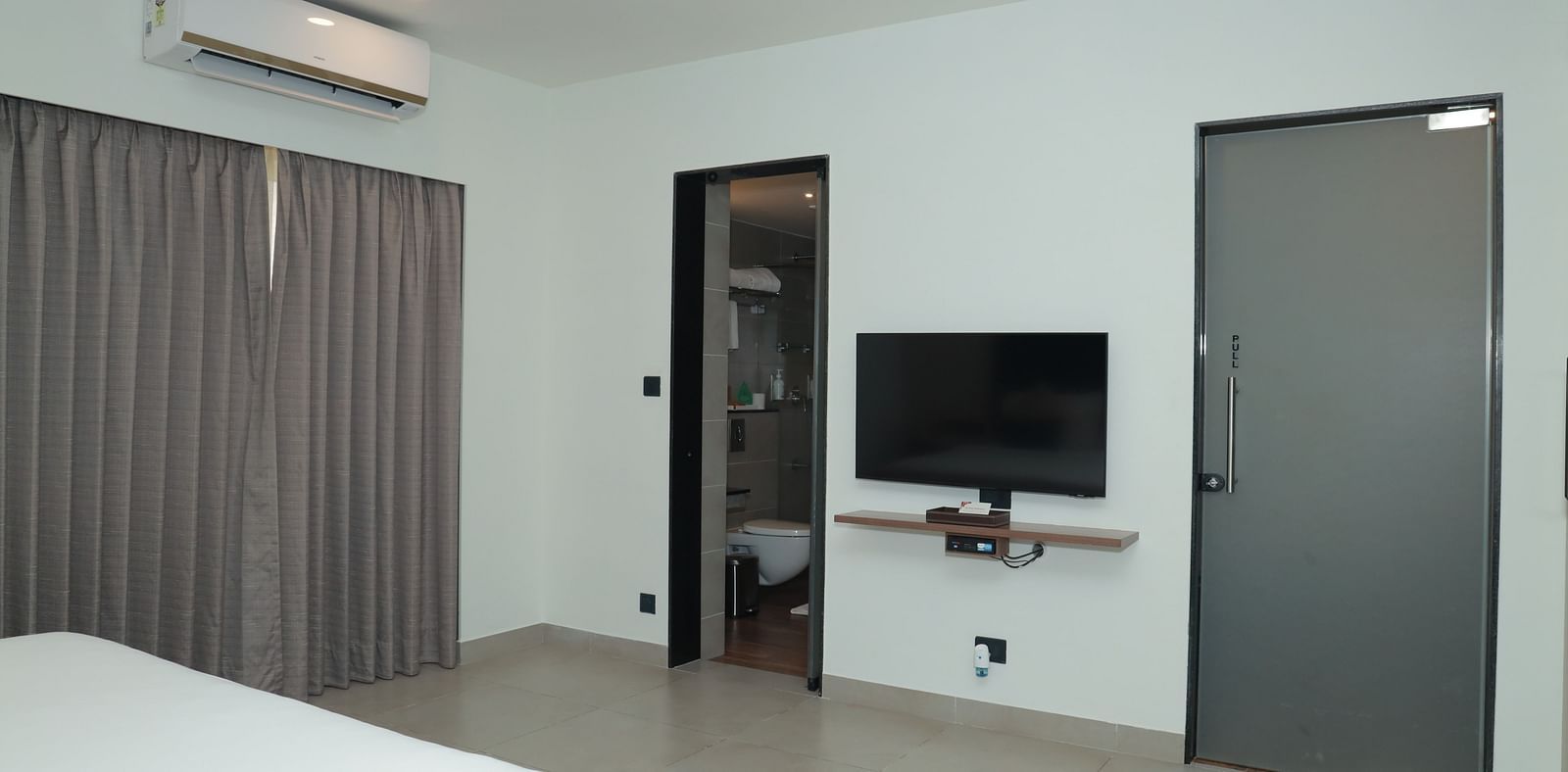 An image of a television mounted on the wall in our suite, with a door opening to the washroom beside it - Regency Tuticorin by GRT Hotels