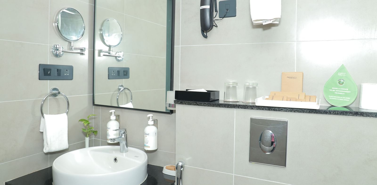 An image of a vanity counter in our suite room, featuring a large sink, a wall-mounted mirror, and a telephone attached to the wall - Regency Tuticorin by GRT Hotels
