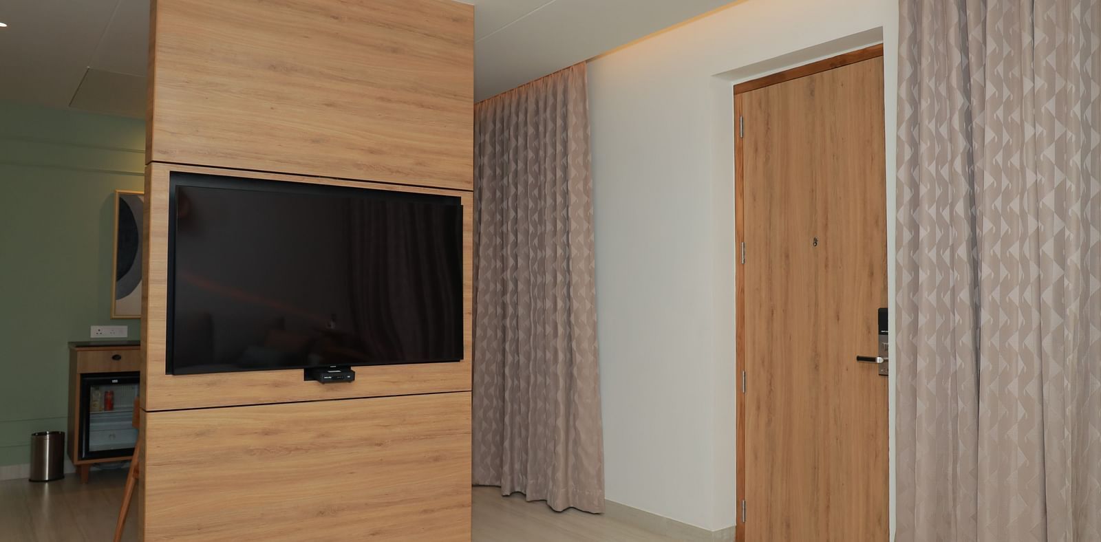 An image of a mounted television with wooden framing around it and a door on the right - Regency Tuticorin by GRT Hotels