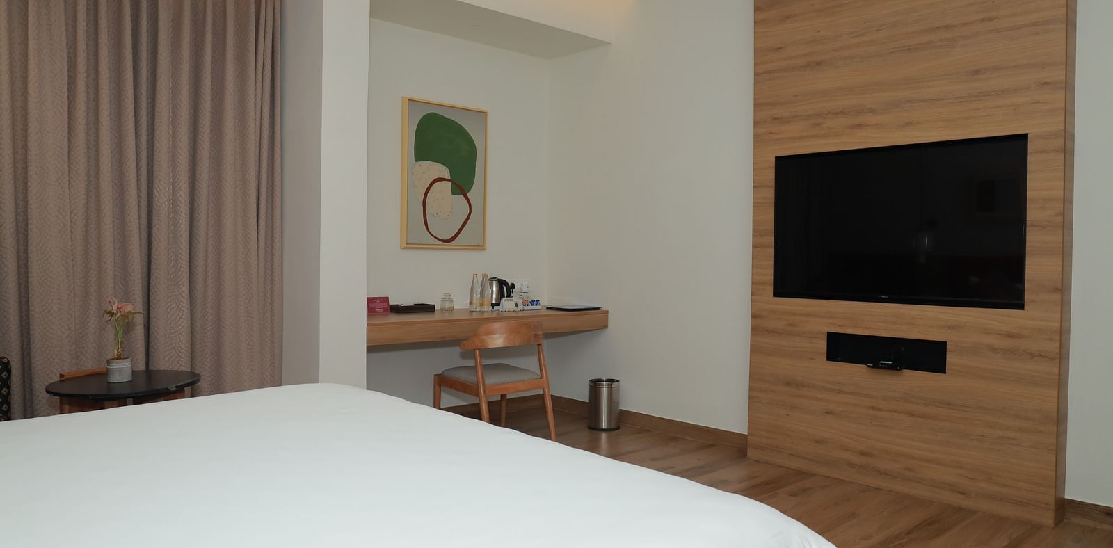 A family room in thoothukudi with a bed, a television and work desk below an abstract wall painting - Regency Tuticorin by GRT Hotels