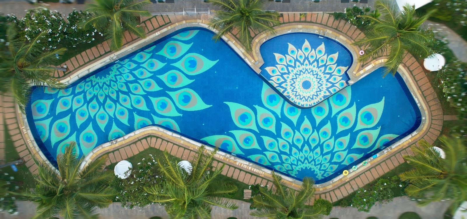 An aerial view of a swimming pool with an intricate blue and white patterned bottom, surrounded by lush greenery | Grand Bay Resort and Spa