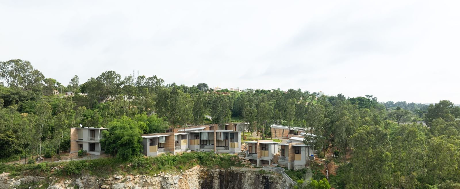 A wide shot of a building complex integrated into a natural, hilly landscape with a body of water visible | Gaia Studio | RD's Nature Retreat, Bangalore