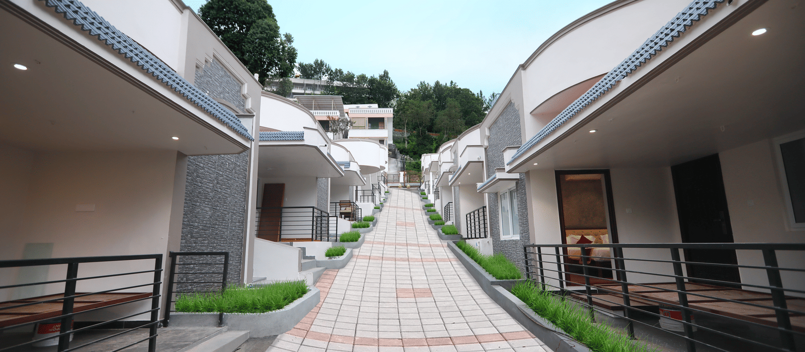 A bright exterior shot of the pathway going upwards at WOW Naturefull Resorts, Yercaud, with cottages on either side of the pathway.
