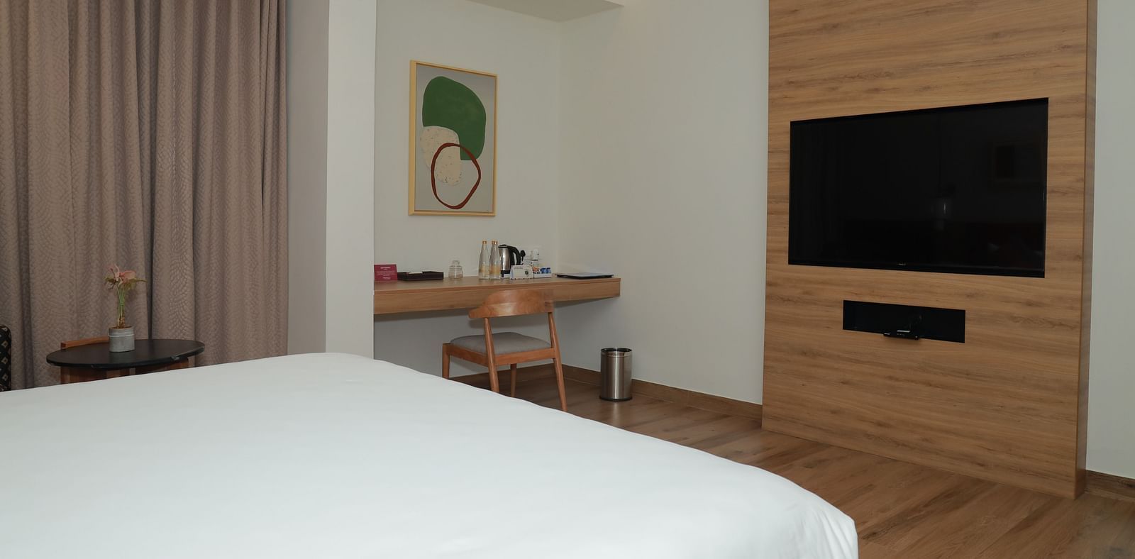 A family room in thoothukudi with a bed, a television and work desk below an abstract wall painting - Regency Tuticorin by GRT Hotels