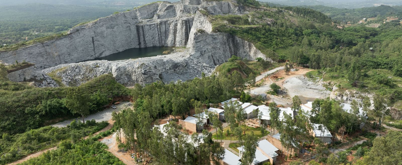 An expansive aerial view showing a large quarry or excavation site with scattered buildings and vegetation | Gaia Studio | RD's Nature Retreat, Bangalore