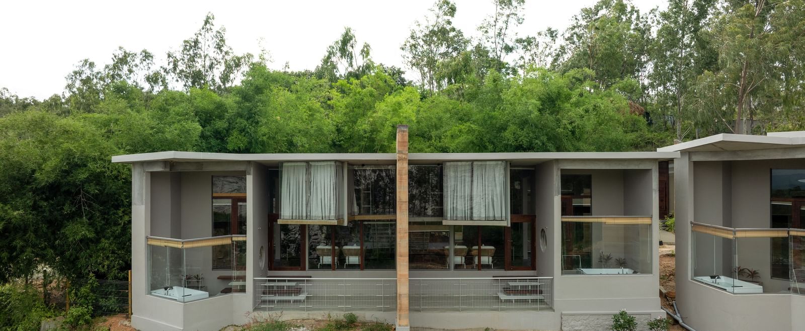 A modern, minimalist building with a flat roof and large windows, surrounded by green foliage under a clear sky | Gaia Studio | RD's Nature Retreat, Bangalore
