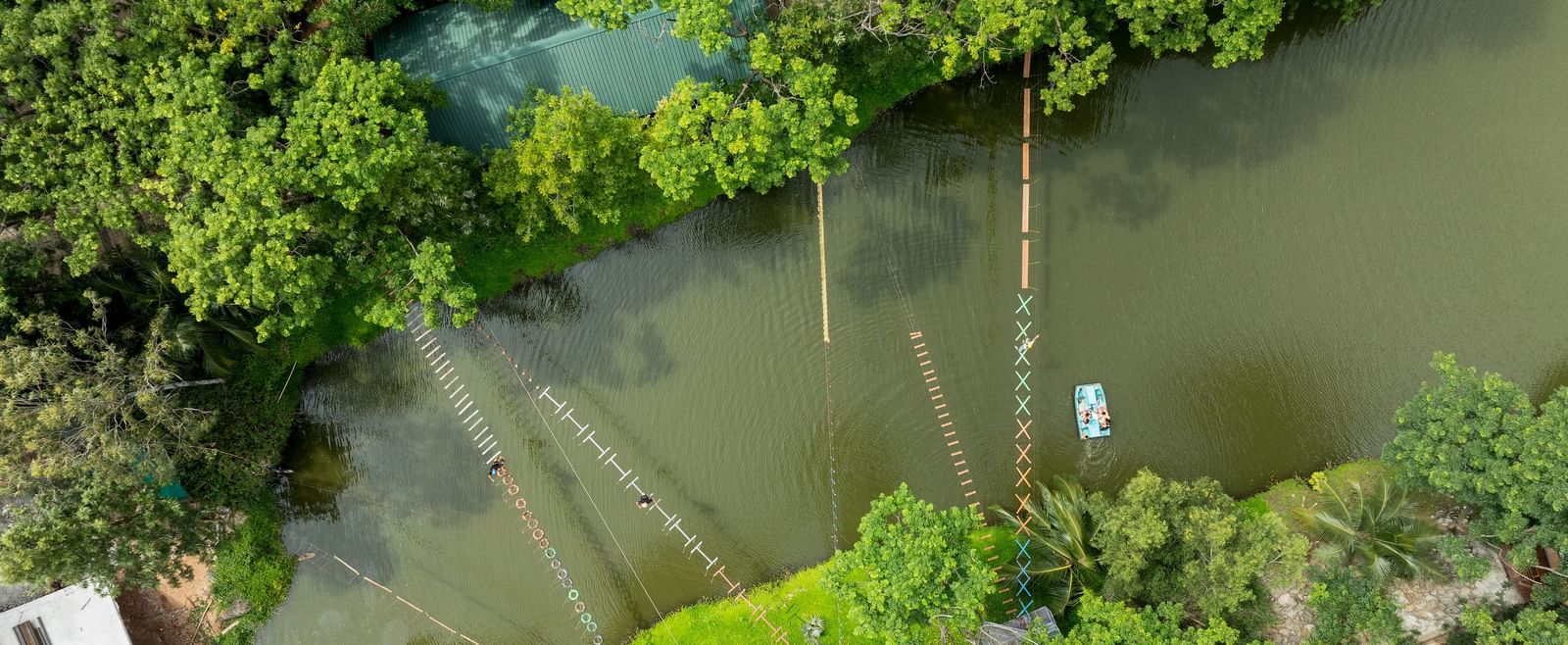 An aerial perspective captures a serene body of water, possibly a river or lake, bordered by vibrant green trees | RD's Nature Retreat, Bangalore