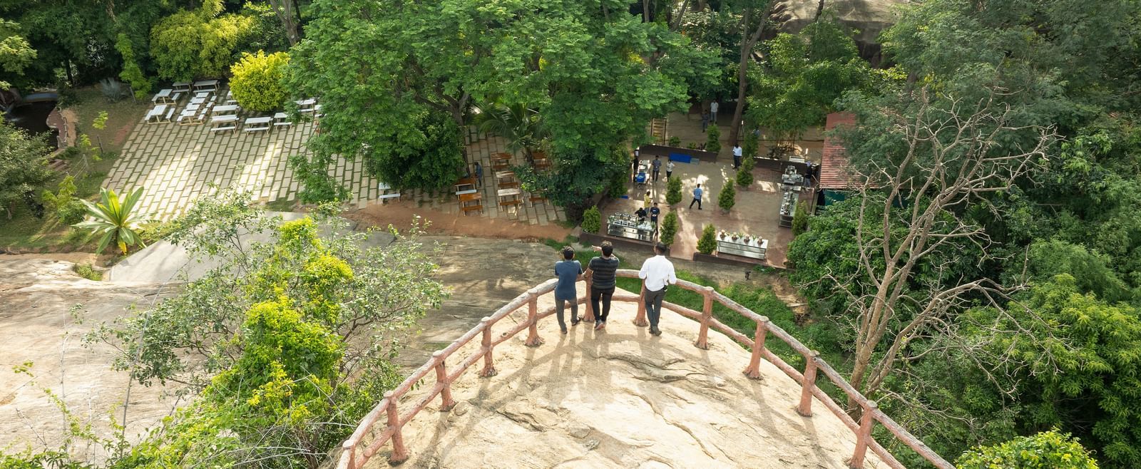 People walk across a rustic wooden bridge elevated above a verdant landscape, likely a bamboo forest or similar natural setting | RD's Nature Retreat, Bangalore