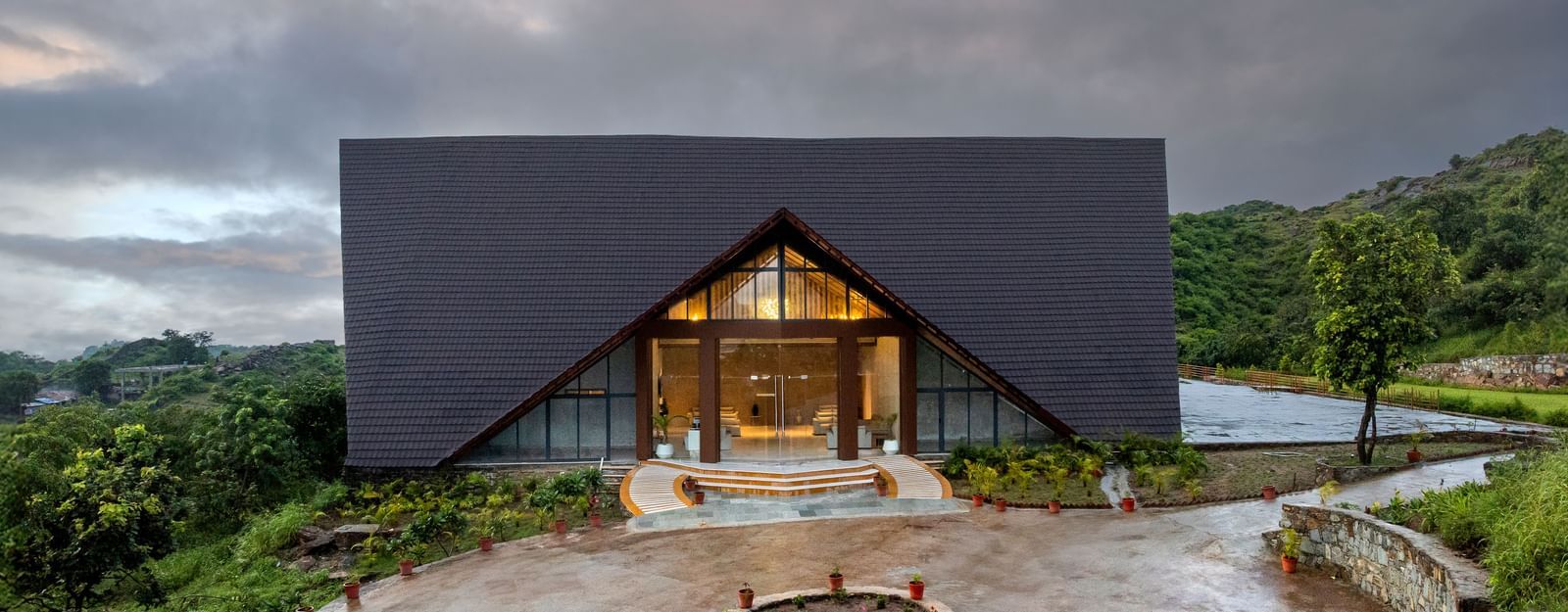 A wide shot of the facade of Osian Valley Resort & Spa, with a large, A-frame entrance and a roundabout with a fire pit in front.