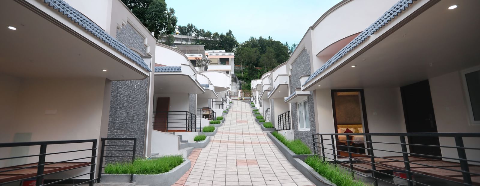 A bright exterior shot of the pathway going upwards at WOW Naturefull Resorts, Yercaud, with cottages on either side of the pathway.