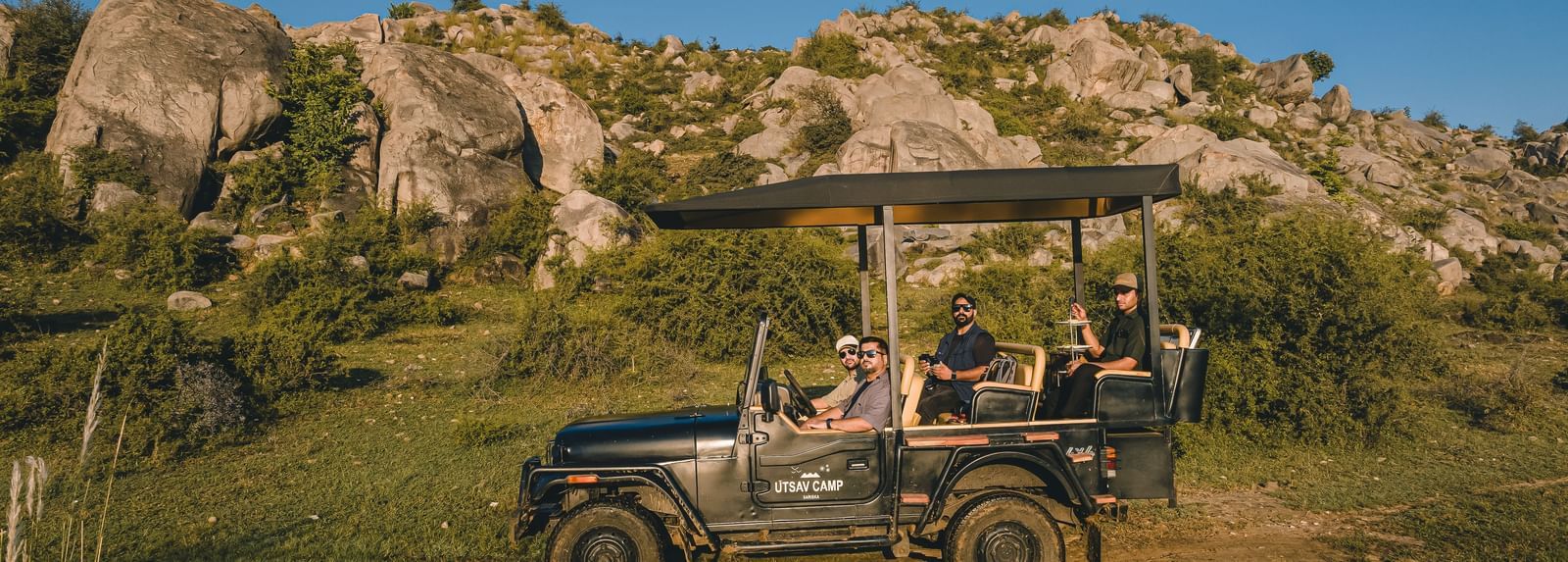 A group of people on a safari jeep with a hill in the background - Utsav Camp Sariska