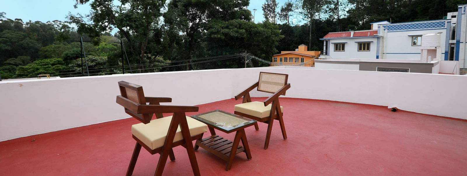 A spacious terrace area at the Terrace cottage with red -coloured flooring, featuring 2 cushioned arm chairs with a coffee table at WOW Naturefull Resorts, Yercaud.
