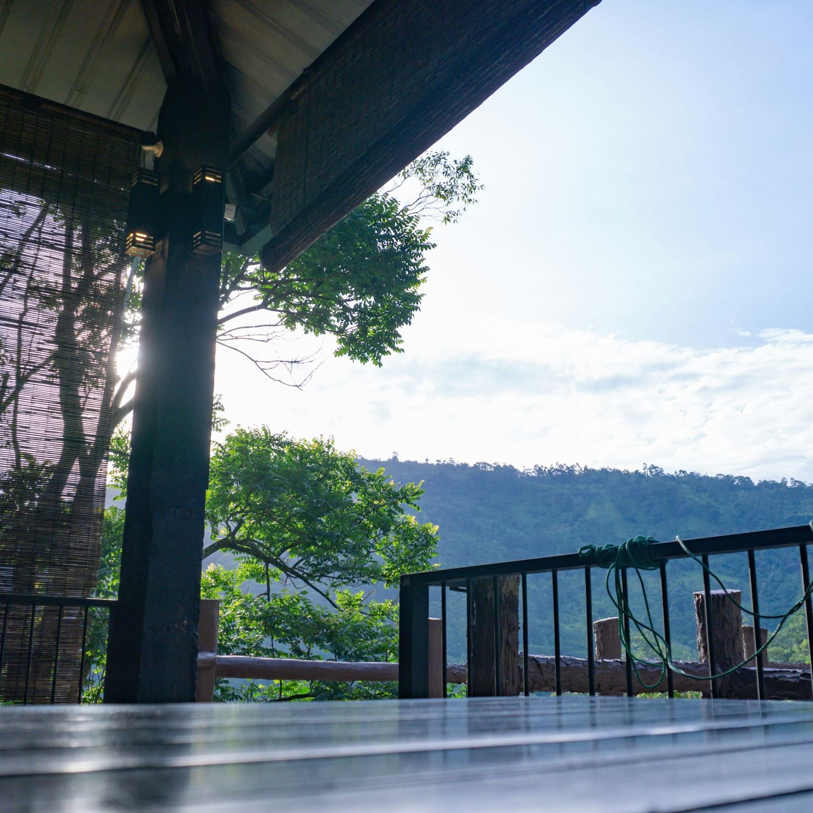 Balcony or terrace area with a wooden roof, railing, and lush green surroundings.
