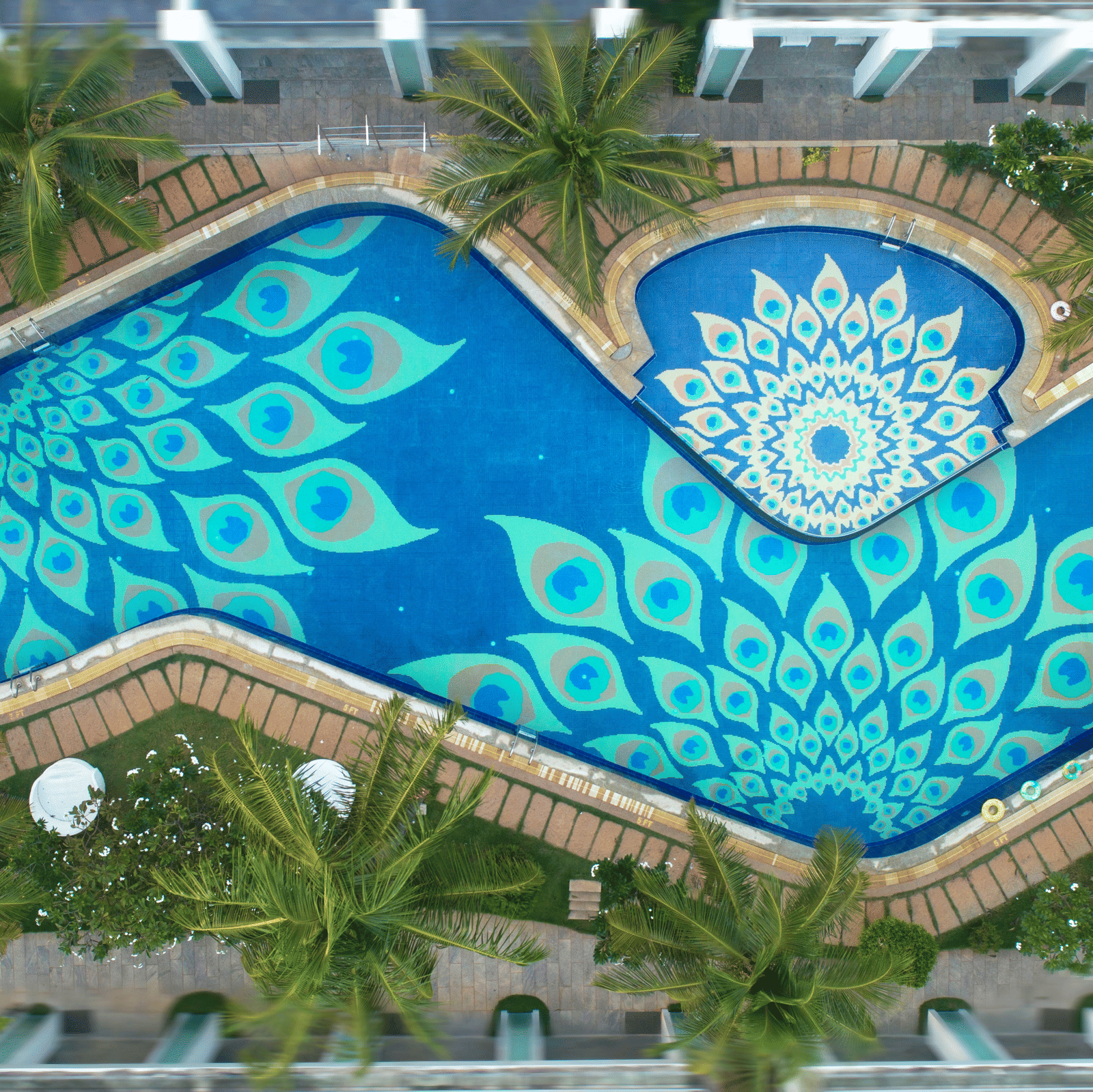 Aerial view of a blue swimming pool designed with decorative patterns surrounded by coconut trees - Grande Bay Resort & Spa, Mamallapuram