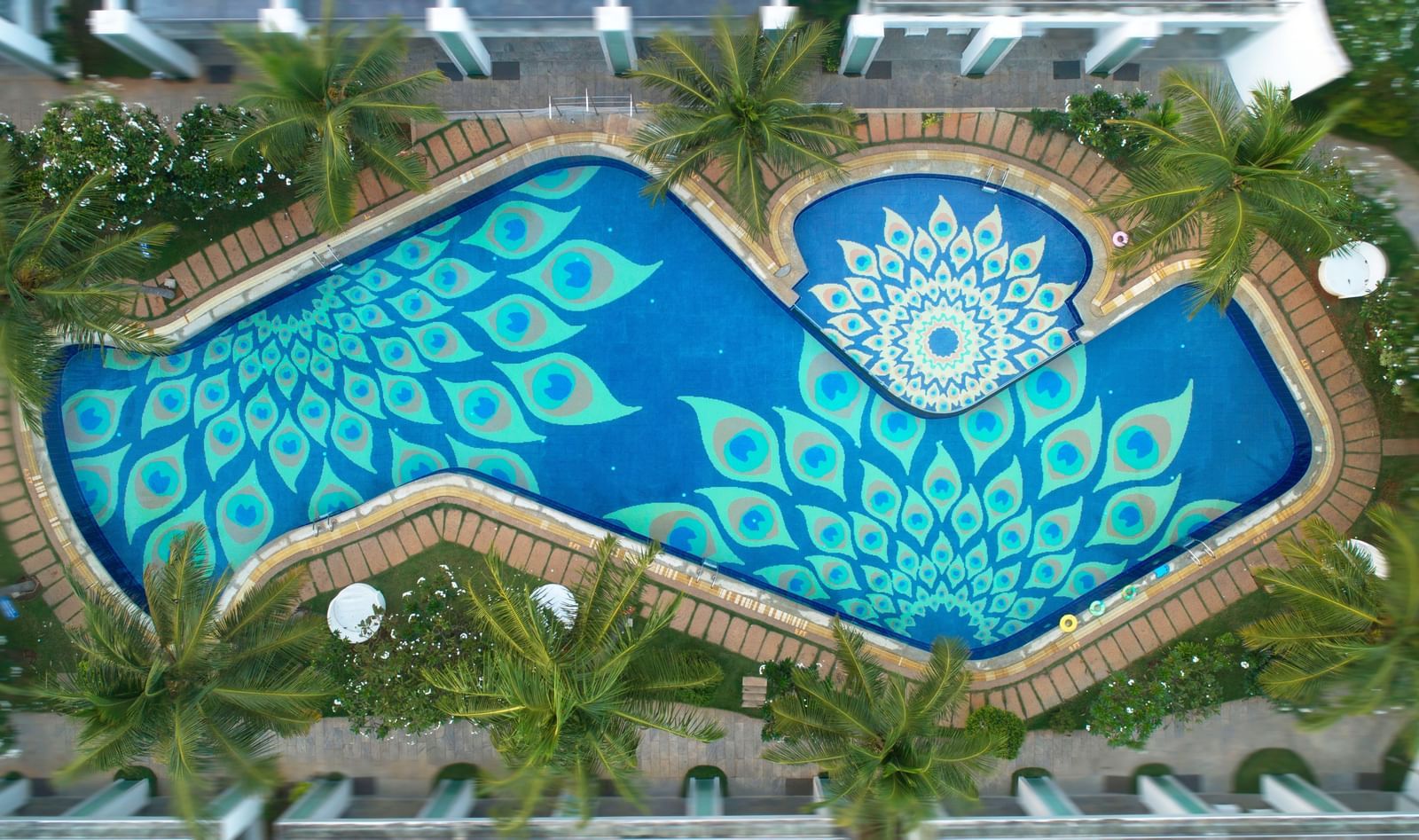 An aerial view of a swimming pool with an intricate blue and white patterned bottom, surrounded by lush greenery | Grand Bay Resort and Spa