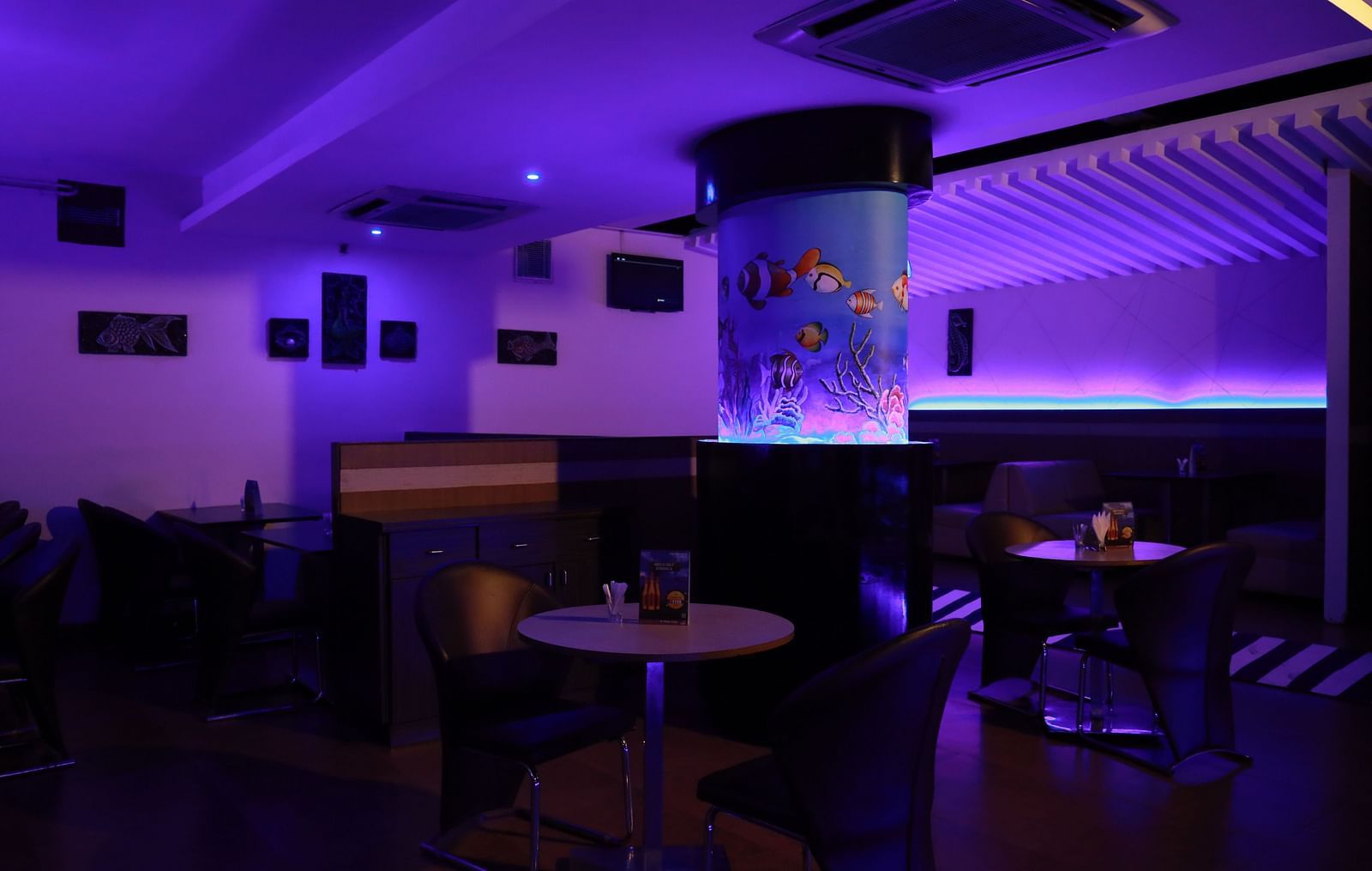 Our bar in Tuticorin, featuring mood lighting, round tables, and a large glass structure representing an aquarium - Regency Tuticorin by GRT Hotels