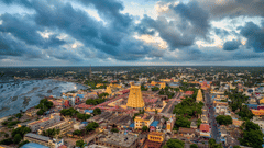 An aerial view of a densely populated city with a large Hindu temple tower (gopuram) dominating the skyline under dark clouds.