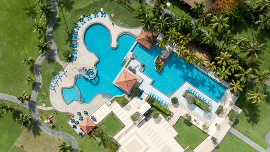 Aerial top-down view of the large swimming pool surrounded by tropical palm trees at Kenilworth Resort & Spa, Goa.