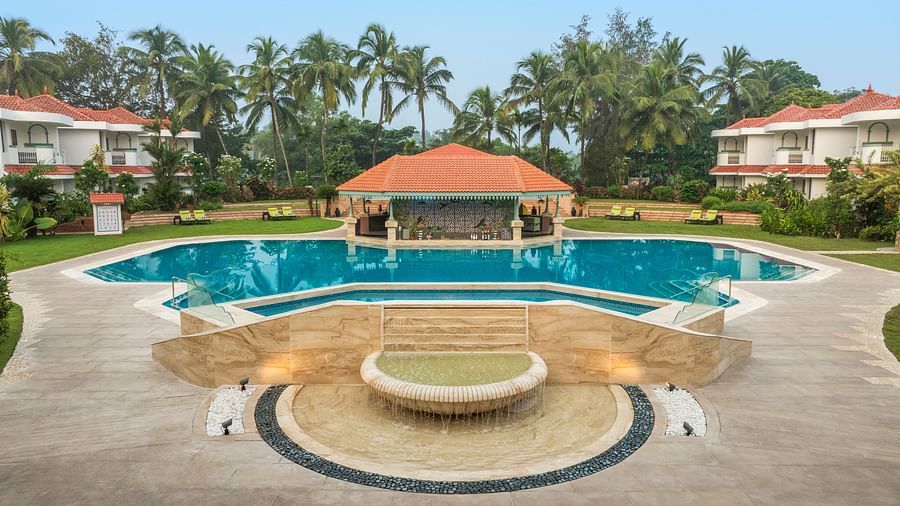 Pool with a shaded pavilion surrounded by palm trees and resort villas.