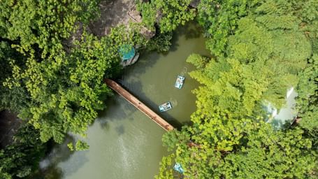 An aerial view shows a boat navigating a narrow, winding river surrounded by lush green foliage | RD's Nature Retreat, Bangalore
