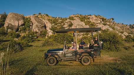 A group of people on a safari jeep with a hill in the background - Utsav Camp Sariska