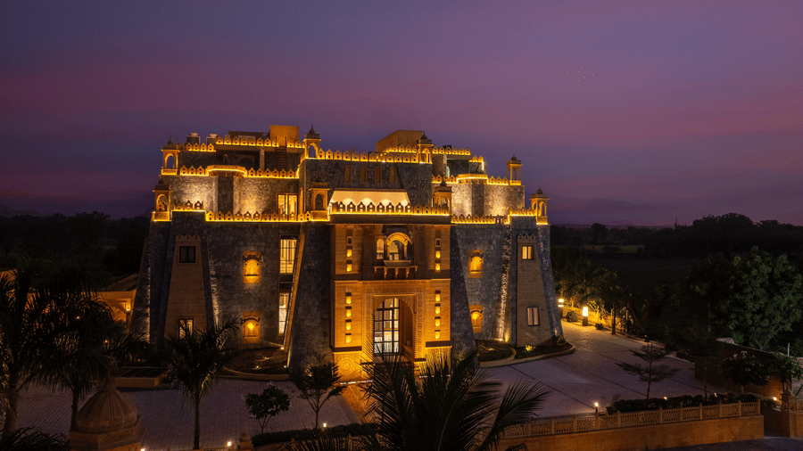 The exterior of EsthereaRaj Leela, Ranakpur, fully illuminated by warm yellow lights against a dark night sky.